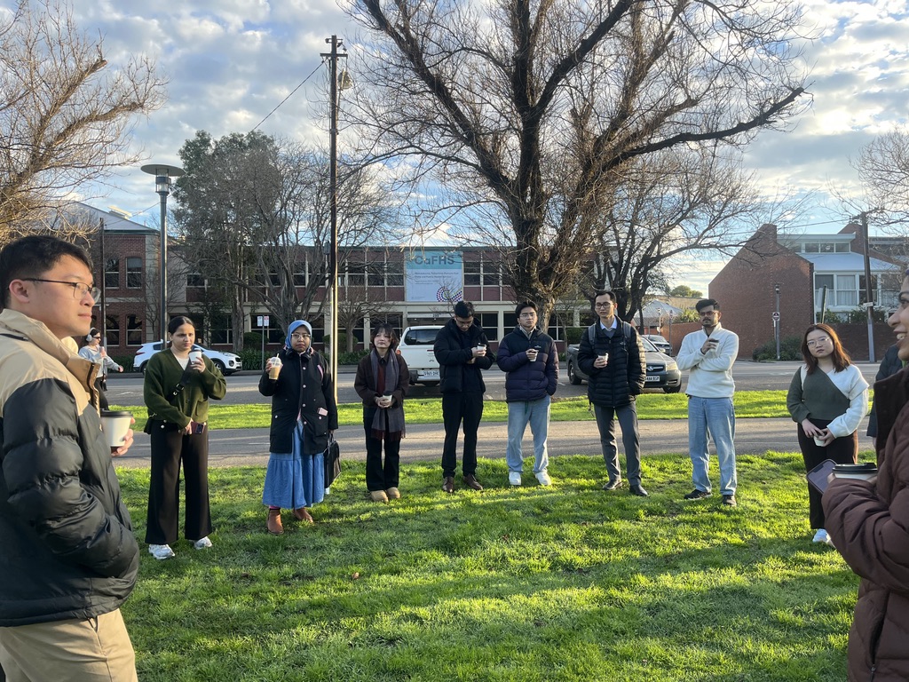 The community standing in a circle on the park lawn with coffee cups