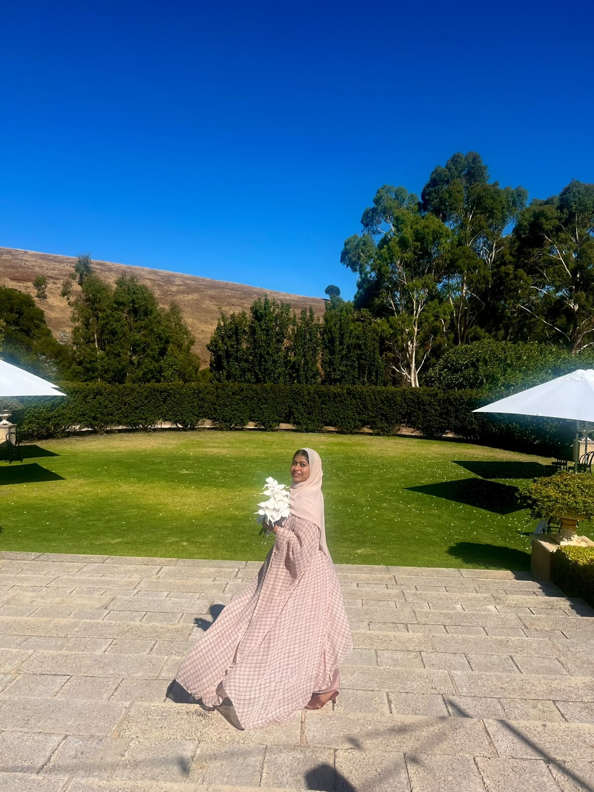 A woman in a pink dress smiling on a sunny lawn